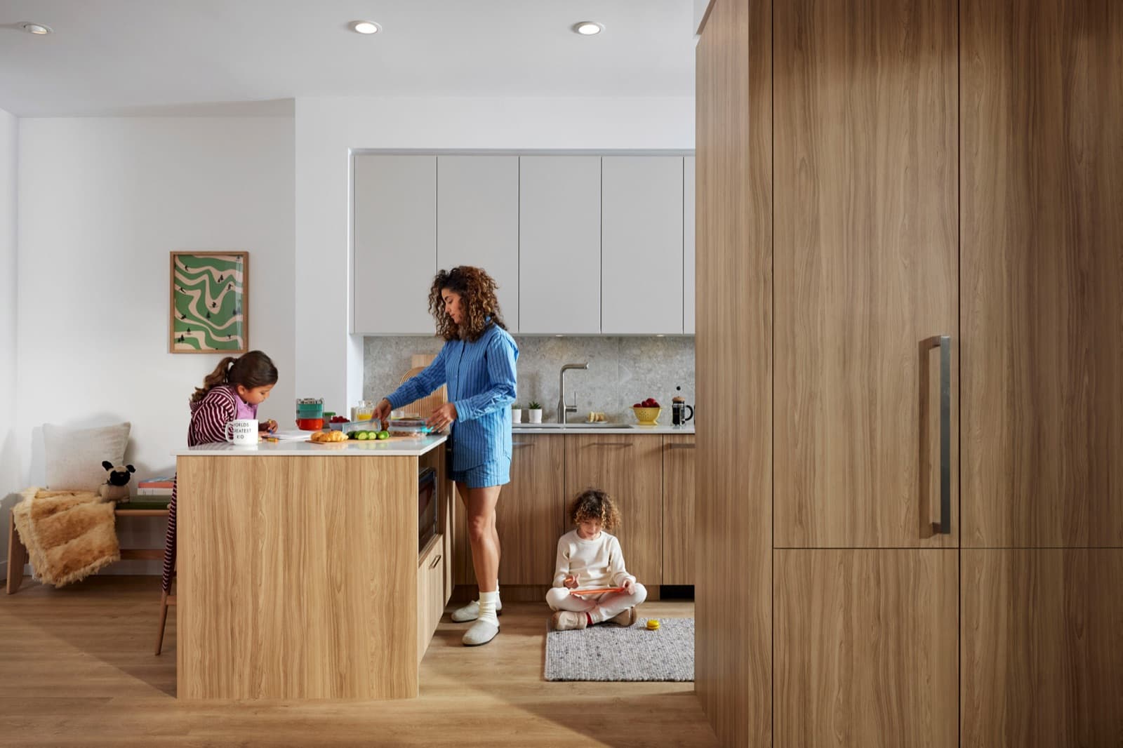 Towns at Lynn – Kitchen with white upper cabinets and a wood island, where a mother prepares food while two children sit nearby.