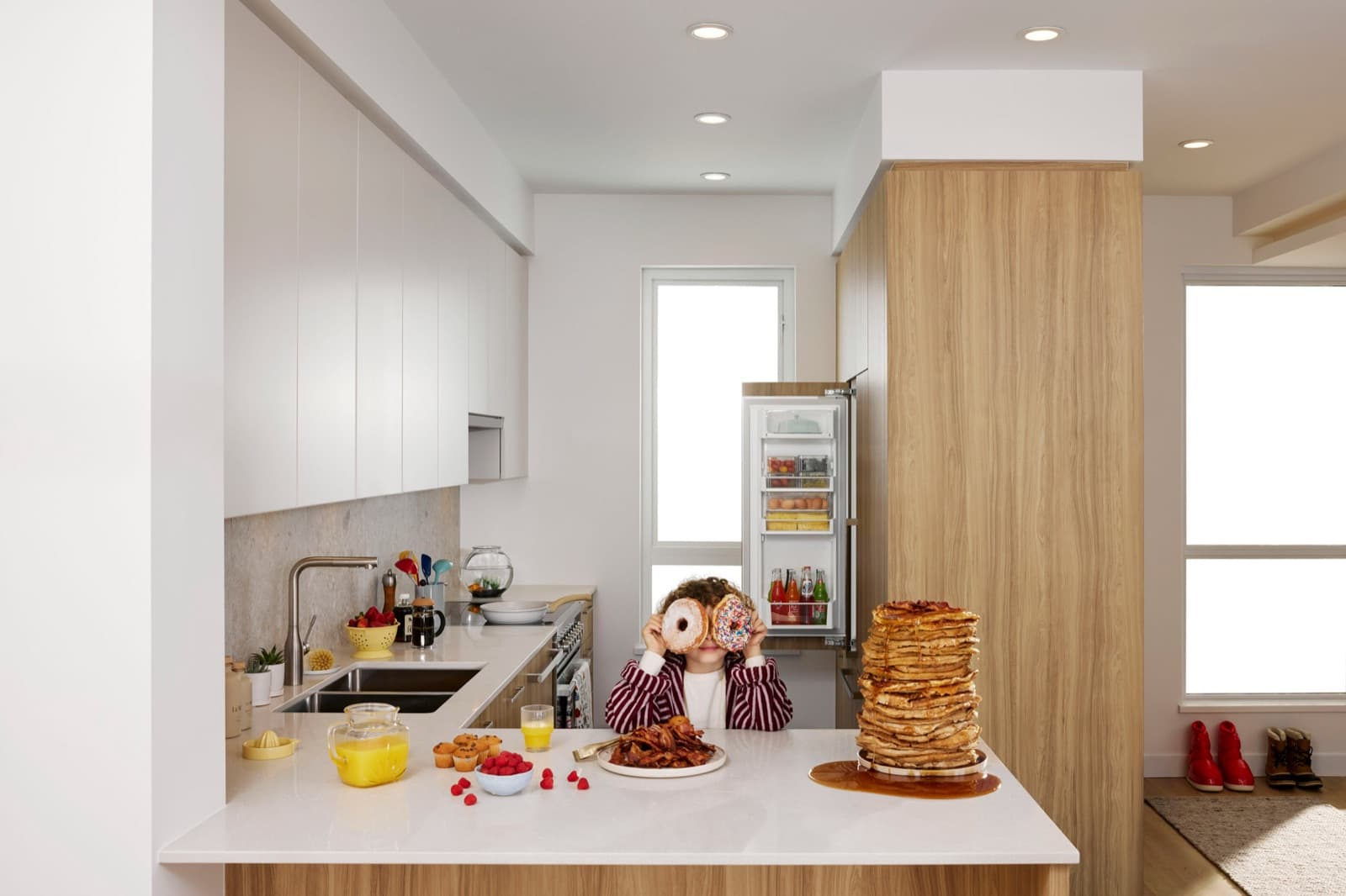 Towns at Lynn – Kitchen counter with a child holding donuts up to her eyes, next to a large stack of pancakes and a breakfast spread.