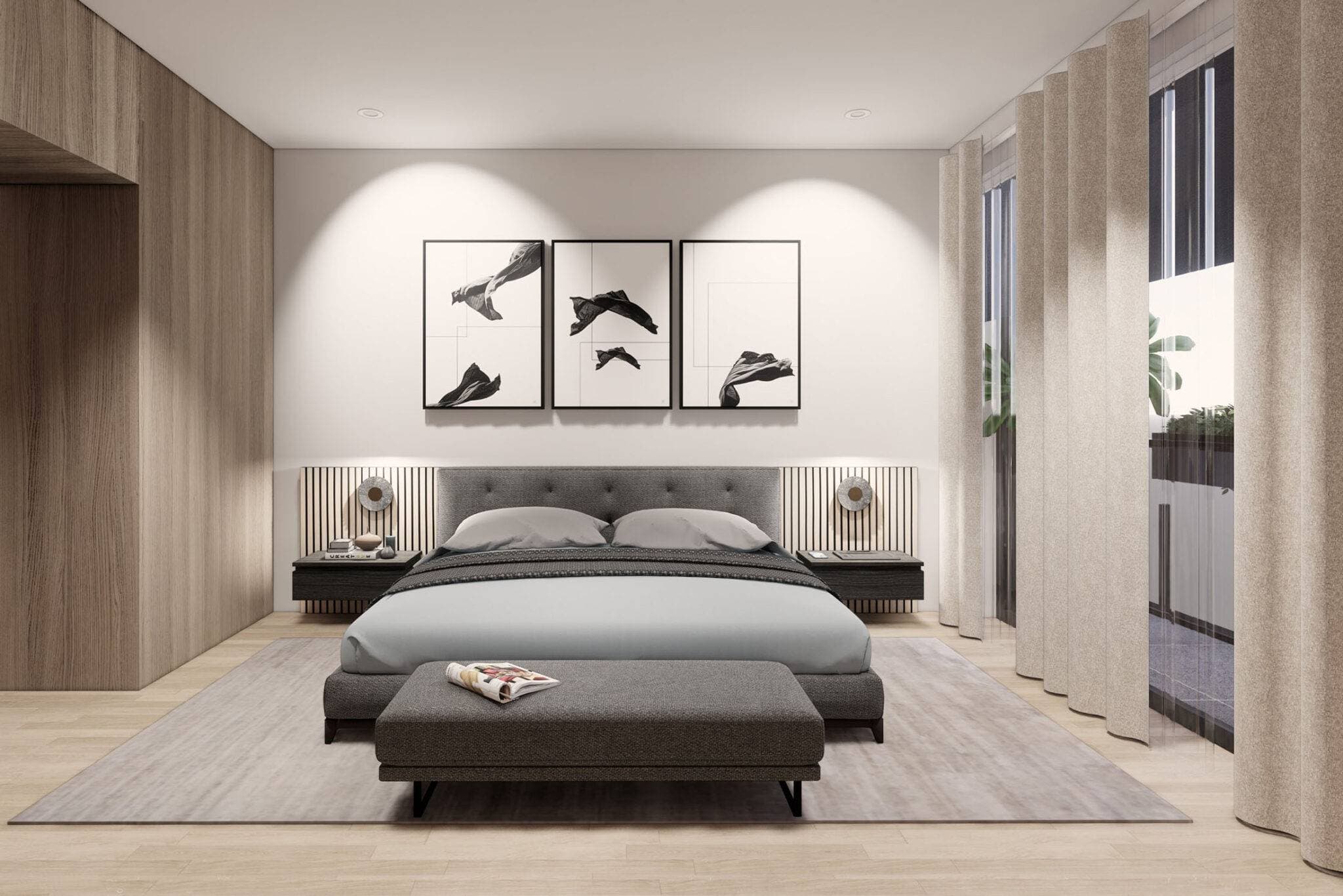 Obsidian on Tenth – A modern bedroom setup featuring a low-profile upholstered grey bed with a matching bench at its foot, set against a backdrop of light wood paneling and three black-and-white art prints. Warm accent lighting illuminates the slatted headboard wall, with floor-to-ceiling drapery framing a window on the right.