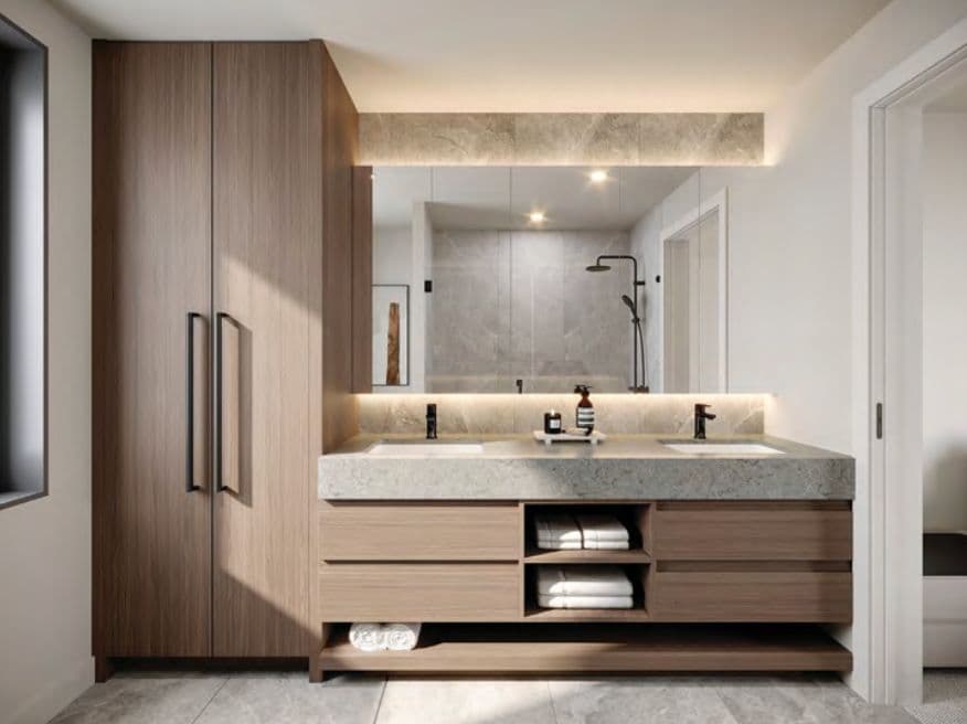 The Edgemont Collection – A bathroom with a stone double vanity, wood cabinetry, a large mirror, and a glass-enclosed shower reflected in the background.