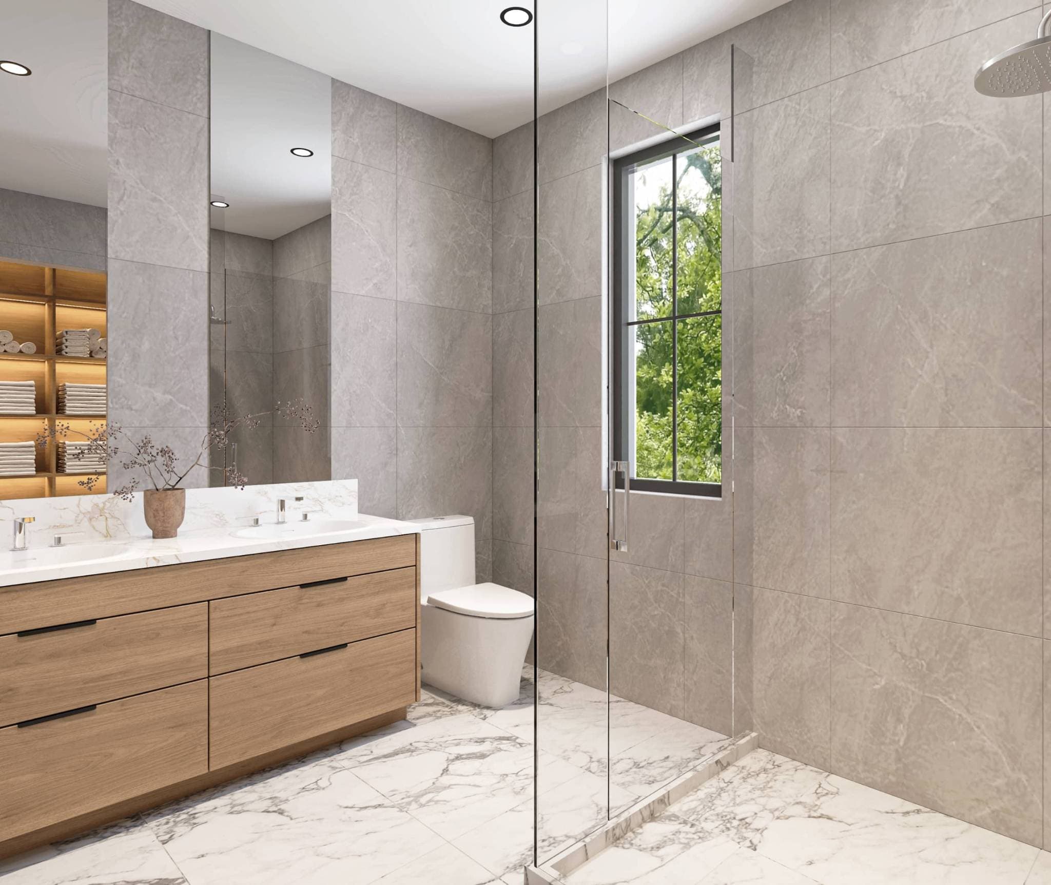 Claremont – A modern bathroom features a glass-enclosed walk-in shower, large grey wall tiles, and white veined marble floor tiling. A floating light wood double vanity with a marble countertop sits beside the toilet, with a black-framed window looking out onto lush green foliage.
