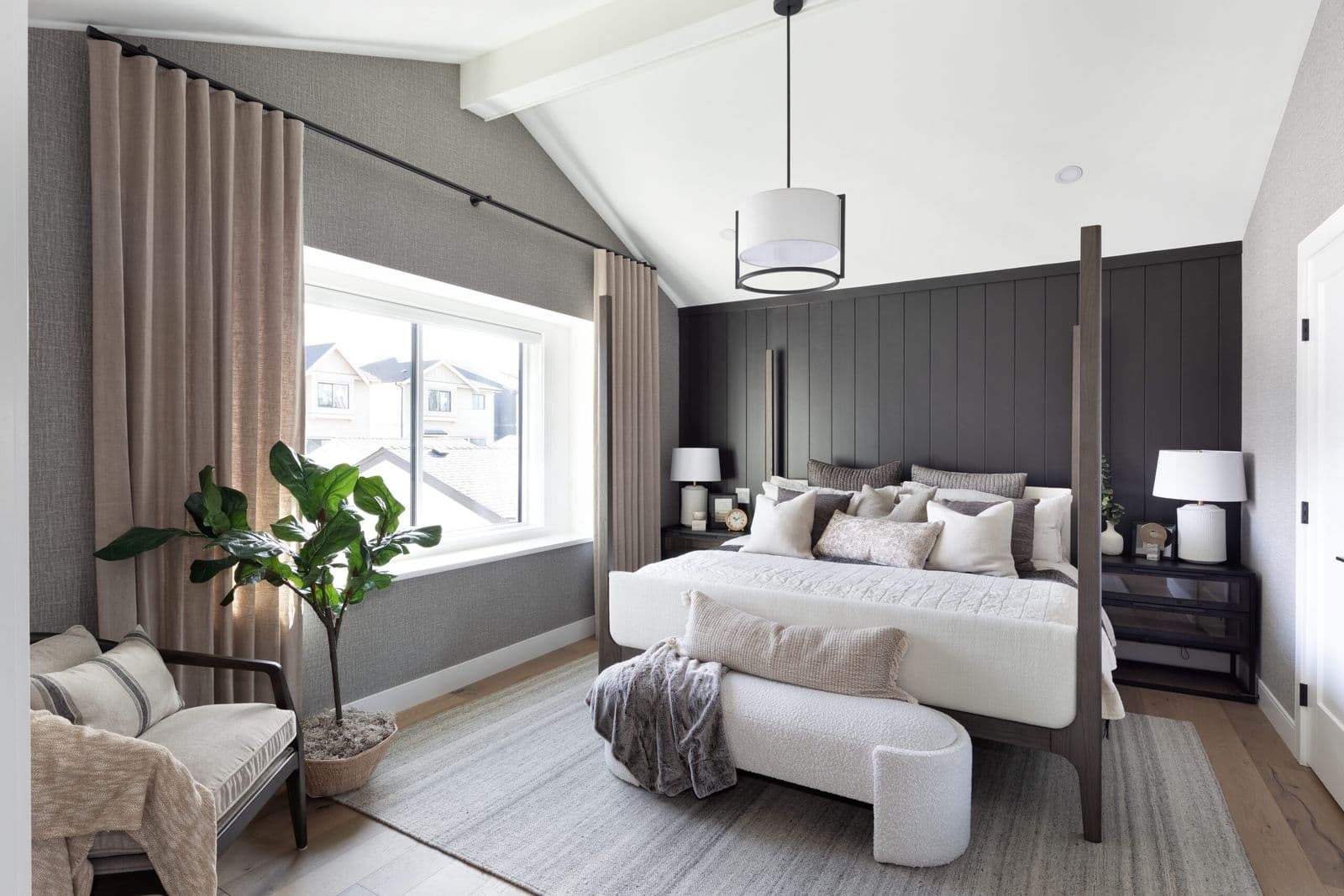 Mirada Estates – Primary bedroom with a dark wood four-poster bed, black shiplap accent wall, upholstered bench, and a window overlooking neighboring rooftops.