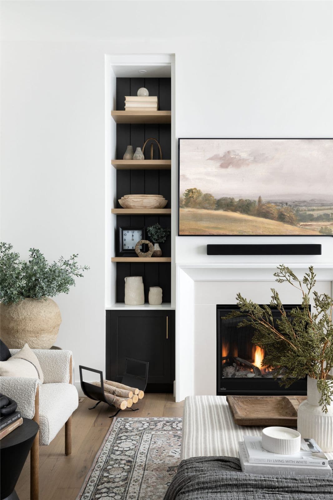 Mirada Estates – Living room with built-in dark wood shelving displaying decor, a wall-mounted TV above a gas fireplace, and a cream armchair.