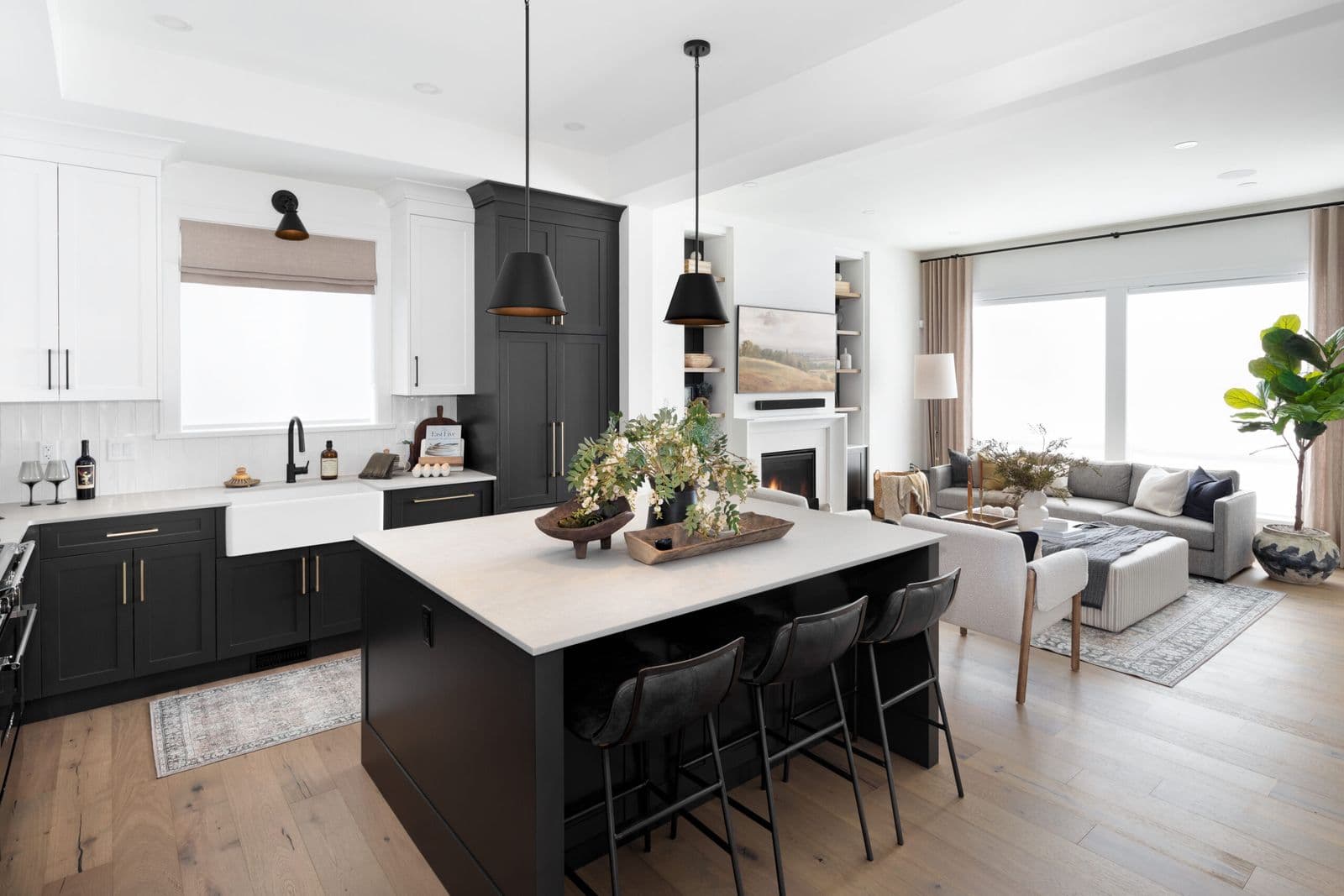 Mirada Estates – Open-concept kitchen with black cabinetry, white countertops, a large island with bar stools, and a view into an adjoining living room.